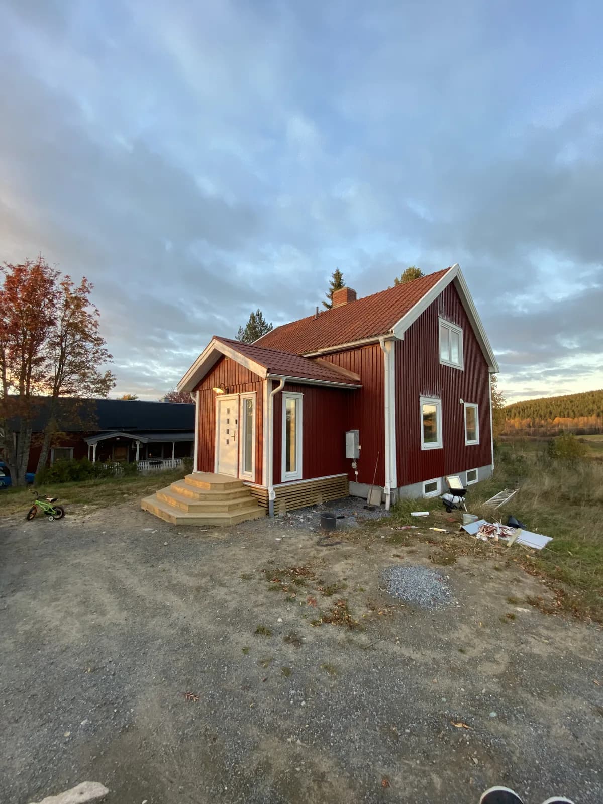 Rött trähus med nybyggda entrétrappor och byggmaterial framför huset