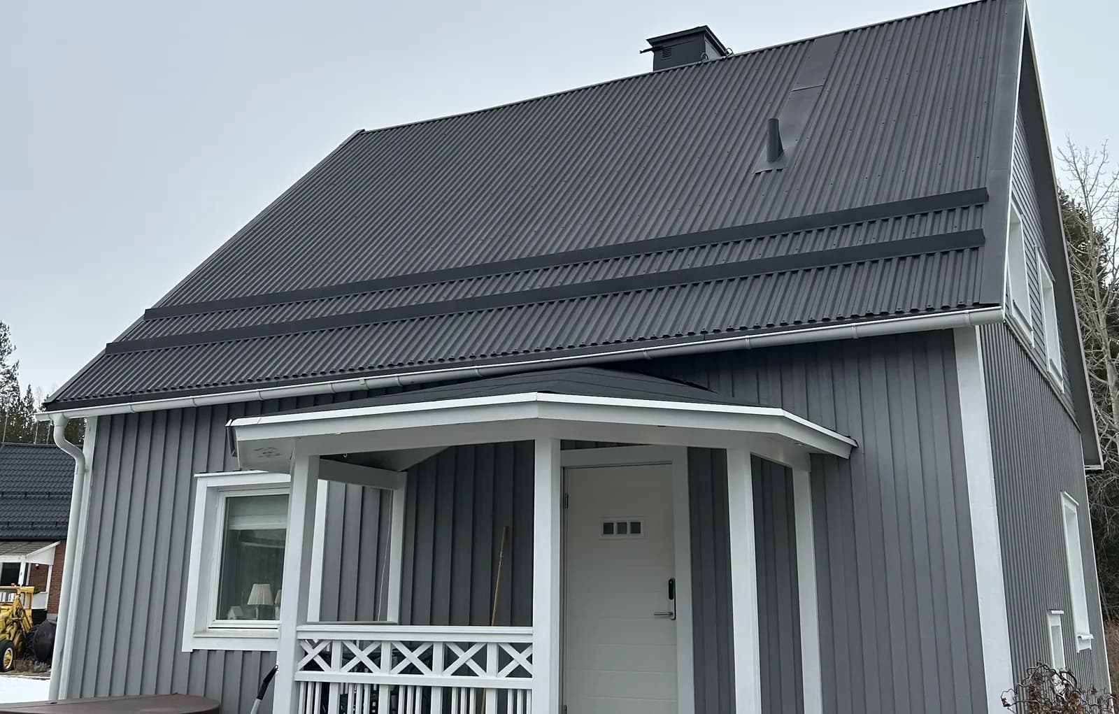 Grå träfasad med vita verandadetaljer och mörkt plåttak
