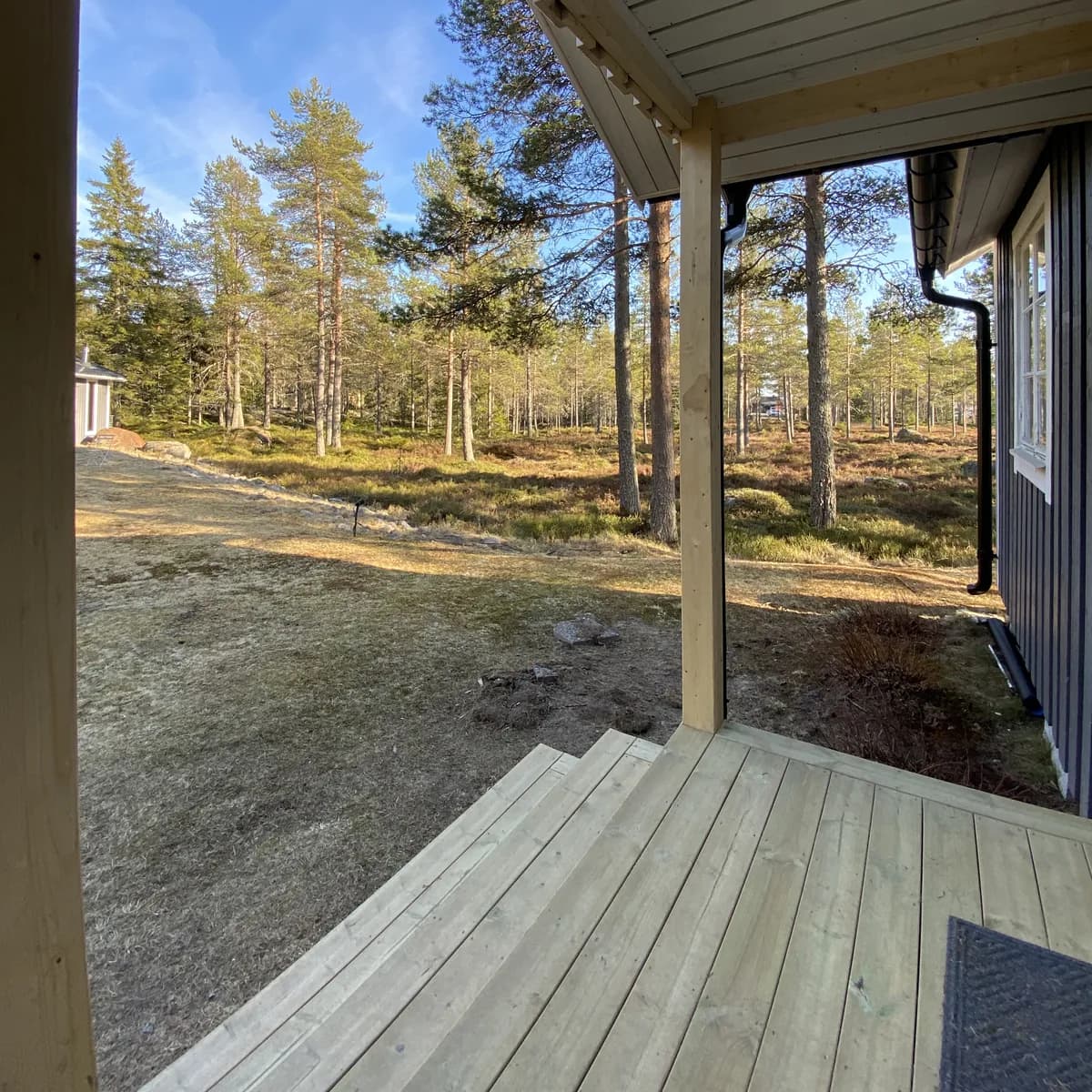 Veranda med trätrall och stolpar med utsikt över tallskog